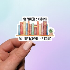 May include: A sticker with a watercolor illustration of a bookshelf filled with colorful books and a small potted plant. The text on the sticker reads "My anxiety is chronic but this bookshelf is iconic."