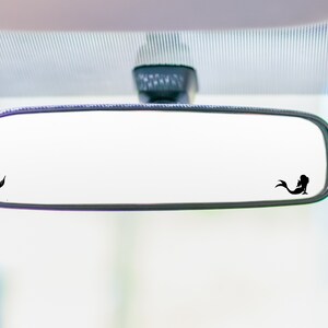 May include: A black rearview mirror with two mermaid silhouettes on the glass. The mermaid silhouettes are facing opposite directions.