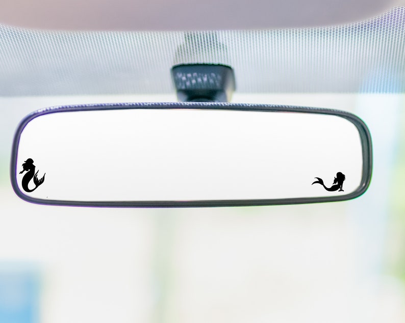 May include: A black rearview mirror with two mermaid silhouettes on the glass. The mermaid silhouettes are facing opposite directions.