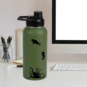 May include: A green reusable water bottle with a black lid and a carrying handle. The bottle has a black silhouette of an octopus, a seahorse, and a shark on the side.