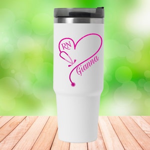 May include: White travel mug with a pink heart design featuring a stethoscope and the text "RN Gianna".