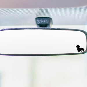 May include: A rearview mirror with a black silhouette of a dachshund dog sticker on the glass.