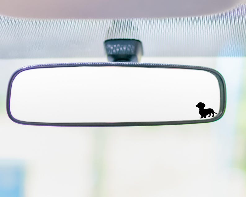 May include: A rearview mirror with a black silhouette of a dachshund dog sticker on the glass.