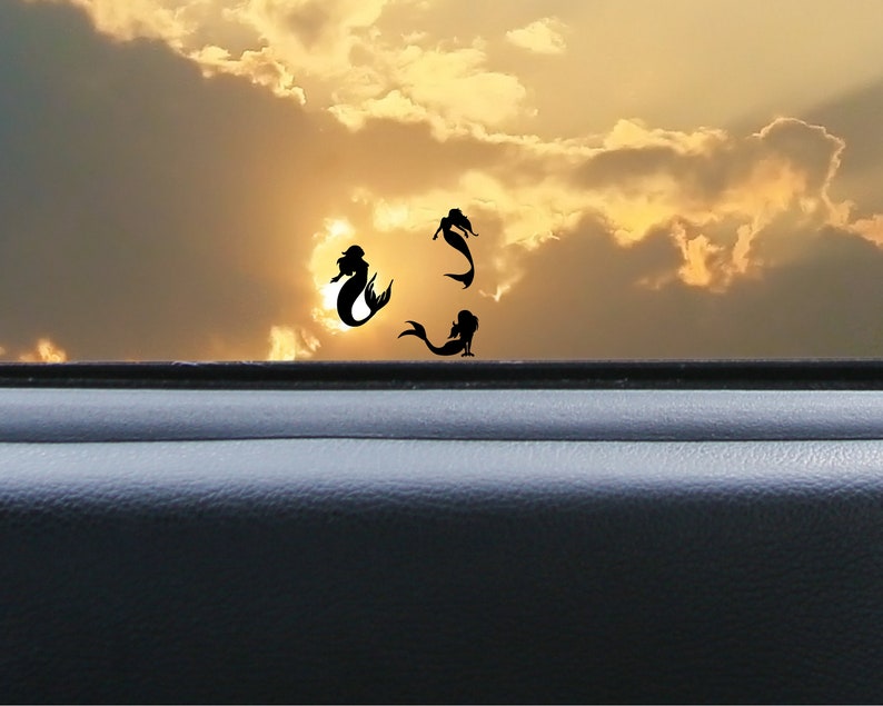 May include: Silhouette of three mermaids against a sunset sky with clouds. The mermaids are facing different directions and appear to be swimming.