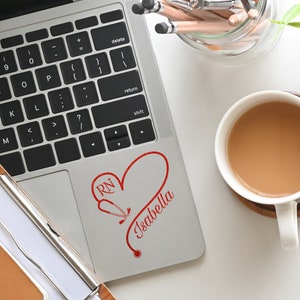 May include: A silver laptop with a red heart and stethoscope design that says "RN Isabella" on the top right corner of the laptop.