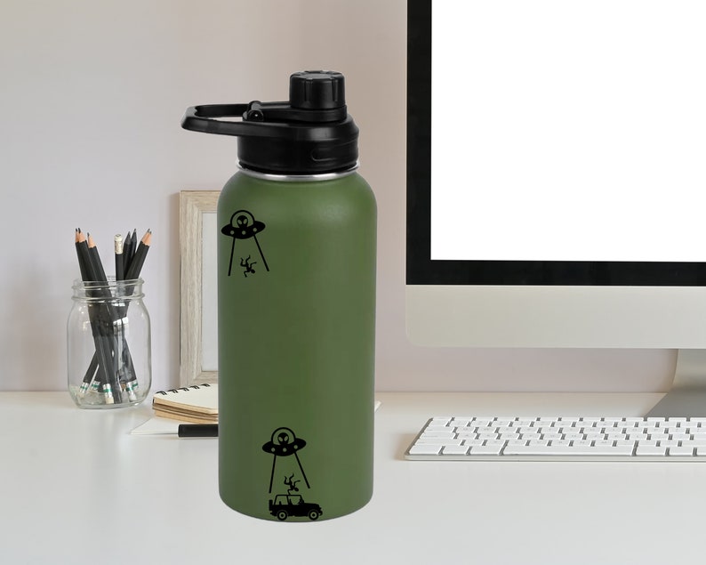 May include: A green reusable water bottle with a black lid and a black and white graphic of a UFO abducting a car.
