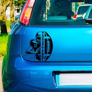 May include: Black and white decal of a football player holding a football with the text "YOUR TEXT" on a blue car.