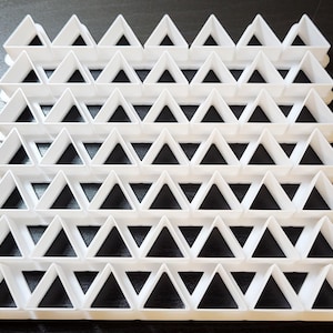 Puede incluir: Molde de plástico blanco con una cuadrícula de 45 formas triangulares. El molde está diseñado para hacer galletas decorativas u otras golosinas.