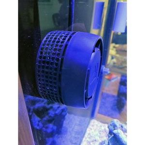 May include: A dark blue aquarium wave maker with a perforated cylindrical section and a solid blue end cap. The wave maker is mounted inside a glass aquarium, with the blue water and rocks visible in the background.