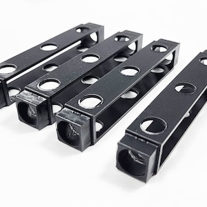 May include: Four black plastic organizers with multiple holes, designed to hold small items like pens, pencils, or tools.