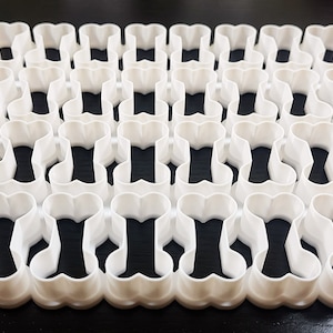 May include: A set of 48 white plastic cookie cutters shaped like bones. The cutters are arranged in a grid pattern.