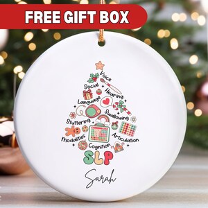 May include: White ceramic Christmas ornament with a colorful illustration of a Christmas tree with speech therapy related icons and the text "SLP Sarah".