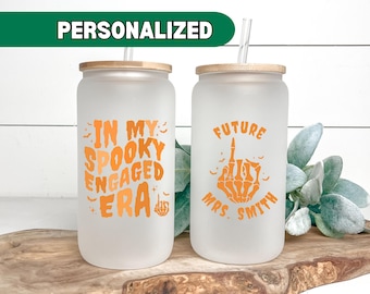 May include: Two frosted glass tumblers with straws. The tumbler on the left says "In My Spooky Engaged Era" in orange text. The tumbler on the right says "Future Mrs. Smith" in orange text with a skeleton hand giving the middle finger.