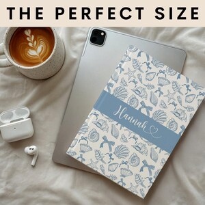 K&ouml;nnte beinhalten: Eine personalisierte Tablet-H&uuml;lle mit einem blau-wei&szlig;en Muschelmuster. Die H&uuml;lle hat ein blaues Band mit dem Namen "Hannah" in Schreibschrift. Der Text "THE PERFECT SIZE" befindet sich oben im Bild.