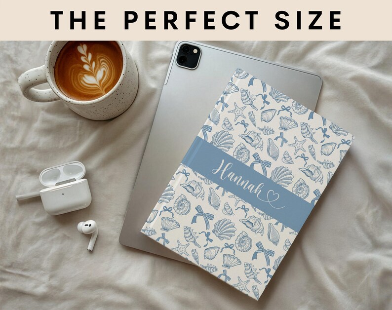 K&ouml;nnte beinhalten: Eine personalisierte Tablet-H&uuml;lle mit einem blau-wei&szlig;en Muschelmuster. Die H&uuml;lle hat ein blaues Band mit dem Namen "Hannah" in Schreibschrift. Der Text "THE PERFECT SIZE" befindet sich oben im Bild.