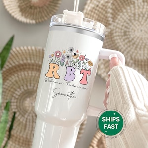 May include: White tumbler with a floral design and the text "RBT Behavior Technician Samantha." The tumbler has a handle and a clear lid with a straw. The design includes colorful flowers and butterflies.