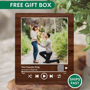 May include: A wooden plaque with a photo of a couple, framed to resemble a music player interface. The photo shows a man kneeling in front of a woman. Text on the plaque reads "Your Favorite Song" and "Artist's Name."