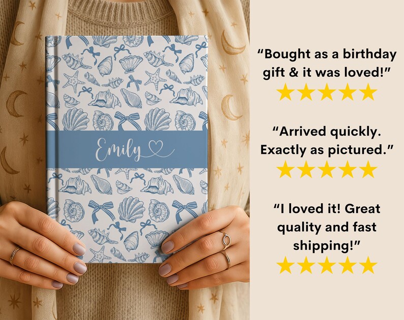 K&ouml;nnte beinhalten: Ein personalisiertes Notizbuch mit einem blau-wei&szlig;en Muschelmuster. Das Notizbuch hat ein blaues Band mit dem Namen "Emily" und einem Herzen. Das Notizbuch wird von einer Person gehalten.