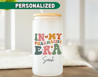 May include: A white frosted tumbler with a bamboo lid and a straw. The tumbler has a colorful graphic that says "In My Pharmacist Era" with a heart and a mortar and pestle. The name "Sarah" is written in cursive below the graphic.