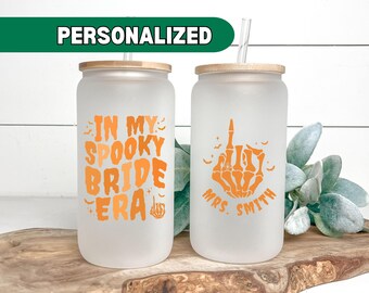May include: Two personalized frosted glass tumblers with lids and straws. One tumbler says "In My Spooky Bride Era" and the other says "Mrs. Smith" with a skeleton hand giving the middle finger.