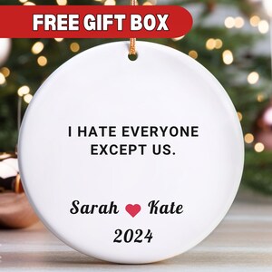 May include: White ceramic Christmas ornament with the text "I hate everyone except us." and the names "Sarah" and "Kate" with a red heart between them. The year "2024" is printed below the names.