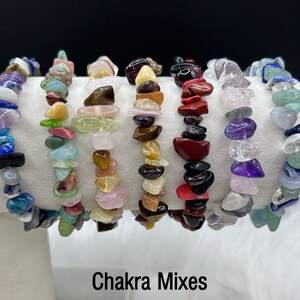 Może przedstawiać: Siedem kolorowych bransoletek wykonanych z małych, odpryskowych kamieni szlachetnych. Bransoletki są ułożone w rzędzie na białym tle. Pod bransoletkami znajduje się napis "Chakra Mixes".