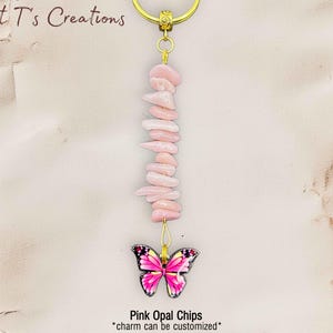 May include: A keychain featuring a strand of pink opal chips, topped with a gold-colored ring and a butterfly charm. The butterfly charm has a pink and black design. The text "Pink Opal Chips" and "charm can be customized" is visible.