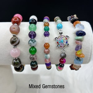 May include: Six colorful gemstone bracelets with a silver turtle charm. The bracelets are made with various stones, including amethyst, rose quartz, tiger's eye, and agate.  Mixed Gemstones.
