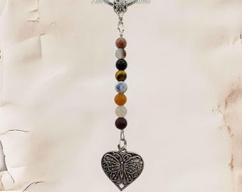 May include: A silver-toned metal keychain featuring a vertical strand of eight multi-colored round beads suspended from a circular ring. At the bottom of the bead strand hangs a silver-toned metal heart-shaped charm with an intricate butterfly design.