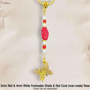 Op de afbeelding: Een goudkleurige sleutelhanger met een rode roos, witte en rode kralen en een vlinderhanger. De bedel is gemaakt met 3 mm rode en 4 mm witte zoetwater schelpen en rode koraal. De tekst luidt "Sweet T's Creations".