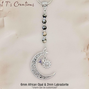 May include: A silver-toned keychain featuring a crescent moon and sun charm, accented with a small star. The keychain is adorned with a string of 6mm African Opal and 2mm Labradorite beads. The text "Sweet T's Creations" is visible at the top.