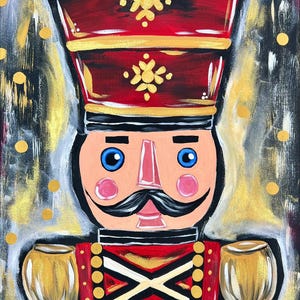 May include: A colorful painting of a nutcracker soldier. The artwork features a red hat with gold accents and a black brim. The soldier has blue eyes, a pink nose and cheeks, and a black mustache. The background is a mix of gold, black, and gray.