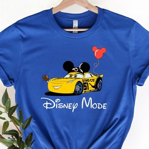 May include: A royal blue t-shirt with a yellow Lightning McQueen car wearing Mickey Mouse ears and holding a red balloon. The text "Disney Mode" is printed below the car.