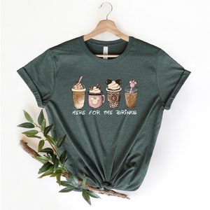 May include: A green t-shirt with a graphic of four different coffee drinks. The text "Here for the drinks" is printed below the drinks.