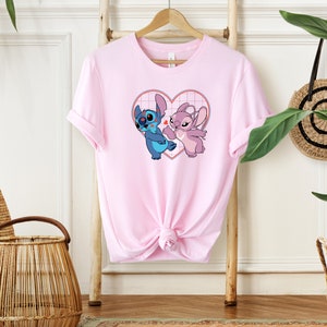 Puede incluir: Camiseta rosa con un gr&aacute;fico de Stitch y Angel de Lilo & Stitch. Los personajes est&aacute;n dentro de un coraz&oacute;n con un patr&oacute;n de cuadr&iacute;cula.
