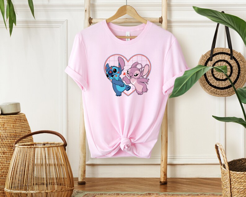 Puede incluir: Camiseta rosa con un gr&aacute;fico de Stitch y Angel de Lilo & Stitch. Los personajes est&aacute;n dentro de un coraz&oacute;n con un patr&oacute;n de cuadr&iacute;cula.