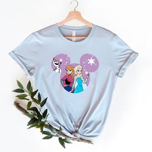 May include: Light blue t-shirt with a purple Mickey Mouse head design featuring the characters Elsa and Anna from Frozen and Olaf.