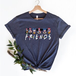 May include: Navy blue t-shirt with a graphic of Mickey Mouse, Minnie Mouse, Donald Duck, Goofy, and Pluto wearing red, white, and blue patriotic hats and sunglasses. The text "FRIENDS" is below the characters.