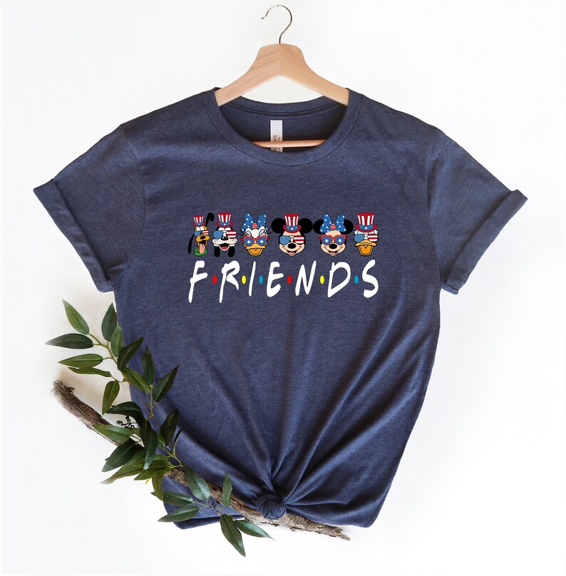 May include: Navy blue t-shirt with a graphic of Mickey Mouse, Minnie Mouse, Donald Duck, Goofy, and Pluto wearing red, white, and blue patriotic hats and sunglasses. The text "FRIENDS" is below the characters.