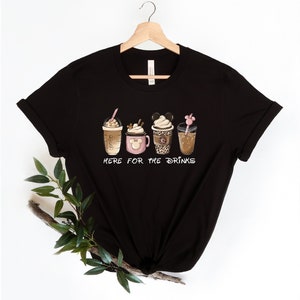 May include: Black t-shirt with a graphic of five different coffee drinks. The text "Here for the drinks" is printed below the drinks.