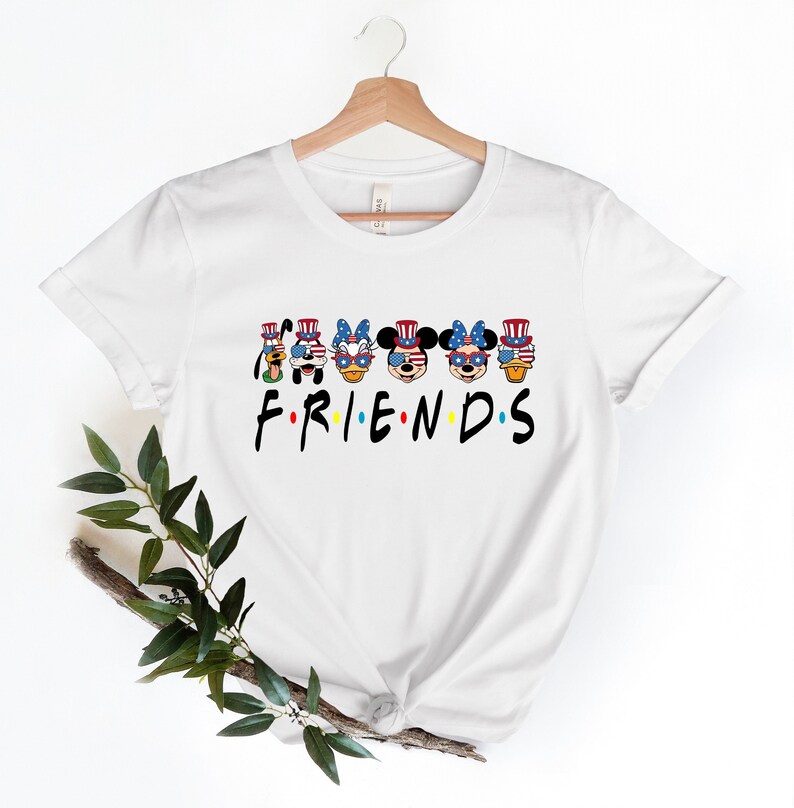 May include: White t-shirt with a graphic of Disney characters wearing red, white, and blue patriotic hats and sunglasses. The text "FRIENDS" is below the characters.