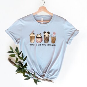 May include: Light blue t-shirt with a graphic of four different coffee drinks. The text "Here for the drinks" is printed below the drinks.