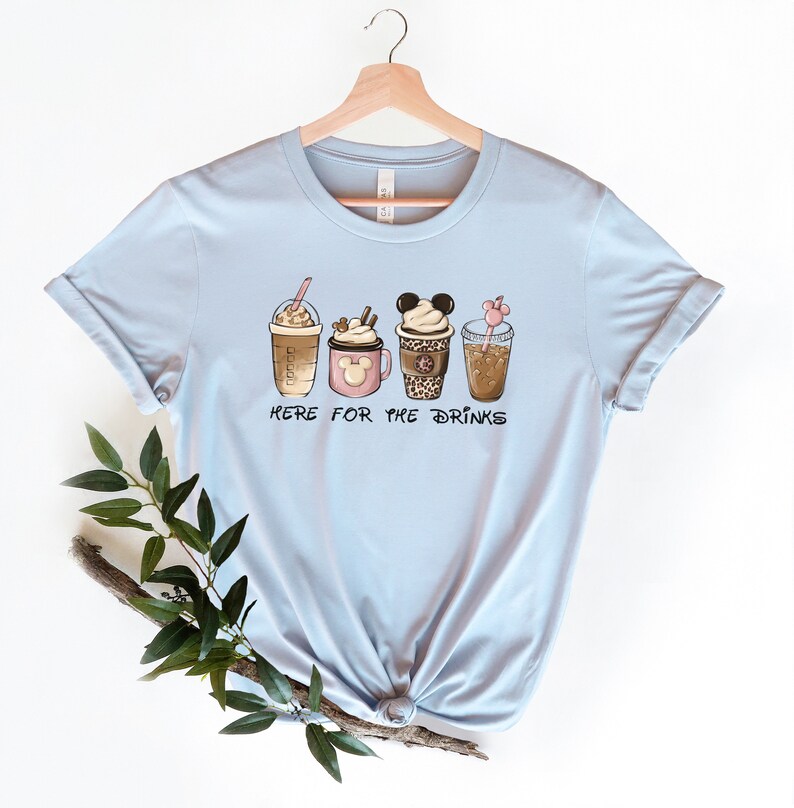 May include: Light blue t-shirt with a graphic of four different coffee drinks. The text "Here for the drinks" is printed below the drinks.