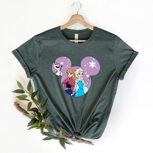 May include: A green t-shirt with a purple Mickey Mouse head design featuring Elsa and Anna from Frozen. Olaf is peeking out from behind them.