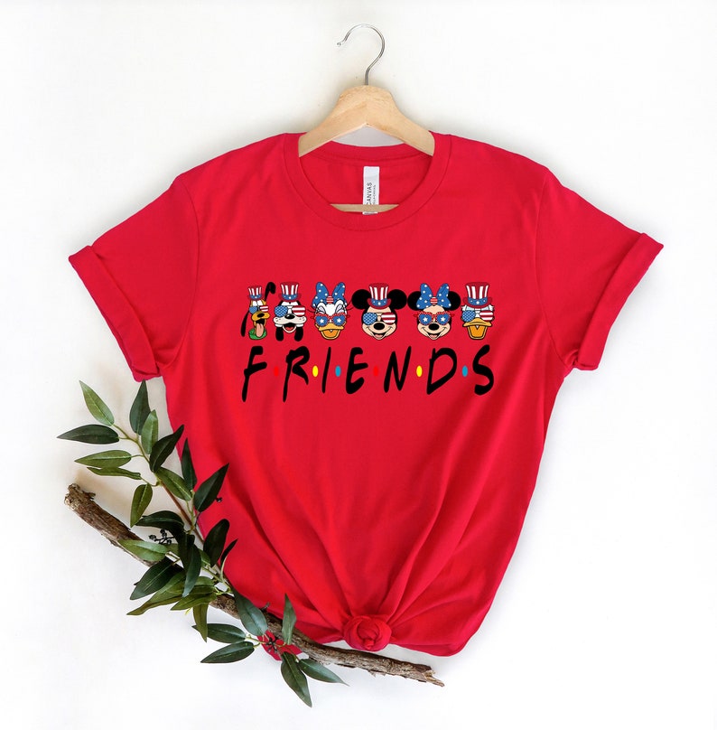 May include: Red t-shirt with a graphic of Mickey Mouse and friends wearing patriotic hats and sunglasses. The text "FRIENDS" is below the graphic.