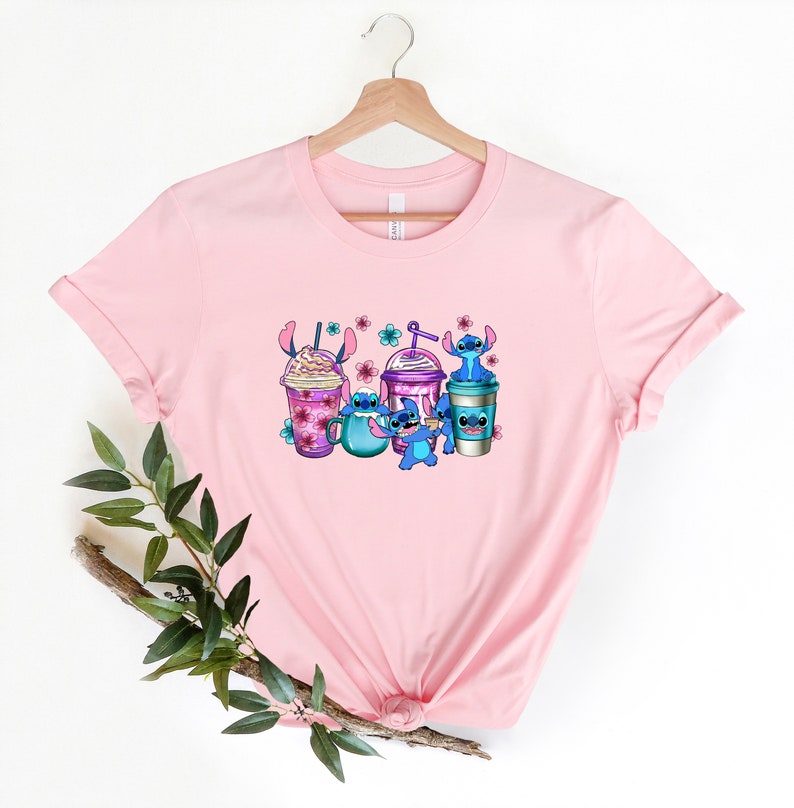 May include: Pink t-shirt with a graphic of Stitch characters holding various colorful iced coffee drinks with pink flowers.