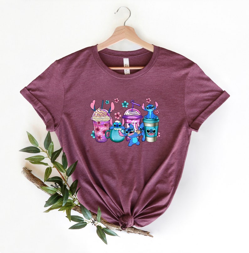 May include: A maroon t-shirt with a graphic of Stitch from Lilo & Stitch holding different coffee drinks. The graphic includes a mocha, a smoothie, and a coffee cup.