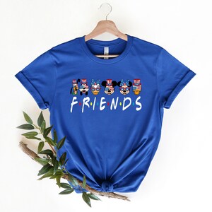 May include: A royal blue t-shirt with a graphic of Mickey Mouse, Minnie Mouse, Donald Duck, Goofy, and Pluto wearing red, white, and blue patriotic hats and sunglasses. The text "FRIENDS" is printed below the characters.