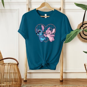 Puede incluir: Camiseta azul turquesa con un gr&aacute;fico de Stitch y Angel de Lilo & Stitch dentro de un coraz&oacute;n. El coraz&oacute;n tiene un patr&oacute;n de cuadr&iacute;cula y corazones rojos.