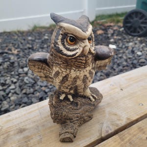 May include: A detailed ceramic owl figurine with outstretched wings, perched on a textured, log-like base. The owl features brown, beige, and cream coloring with orange eyes. The figurine is a decorative item.